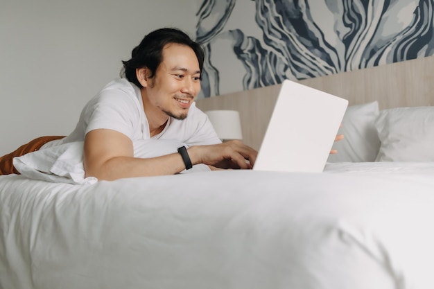 Happy man work with laptop on the bed in the hotel concept of workation