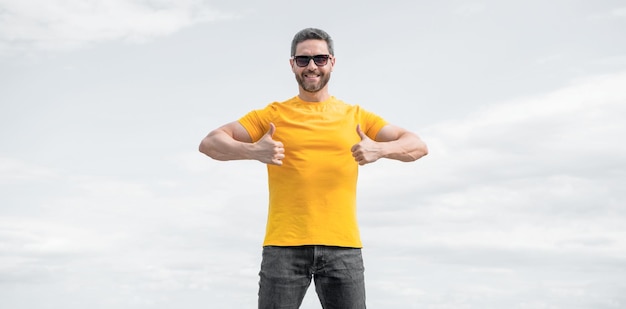 Happy man in yellow shirt and sunglasses on sky background thumb up