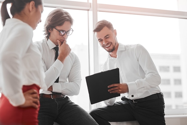 Gestore felice che dimostra i dati negli appunti ai colleghi maschi e femmine mentre discute del progetto di affari vicino alla finestra sul posto di lavoro