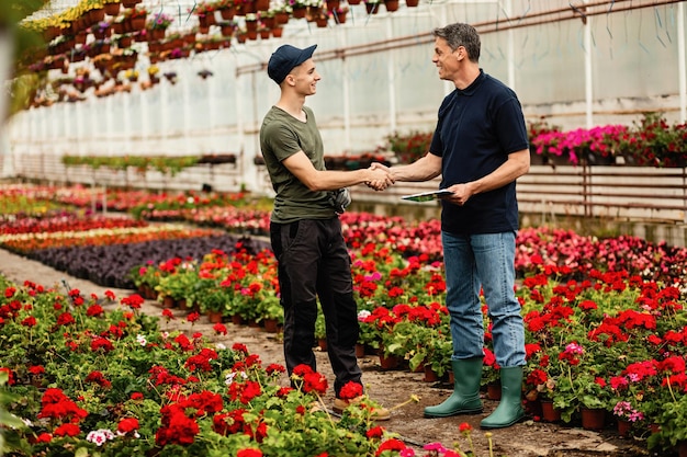 Happy manager shaking hands with young worker while meeting in a greenhouse