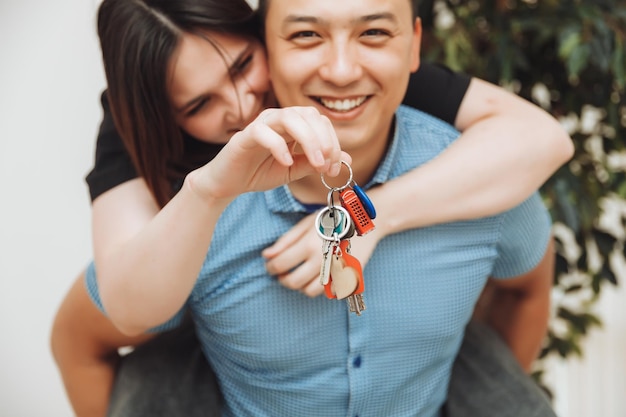 A happy married couple celebrates moving to a new house shows the keys stands in an apartment the concept of a mortgage on real estatekeys closeup