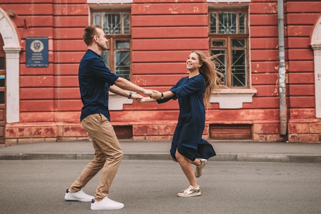 恋をしている幸せな夫婦が通りを駆け下りて喜ぶ。街の通りを歩きながら手をつないで笑顔の美しい若いカップル