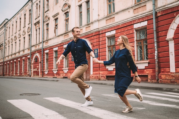 恋をしている幸せな夫婦が通りを駆け下りて喜ぶ。街の通りを歩きながら手をつないで笑顔の美しい若いカップル