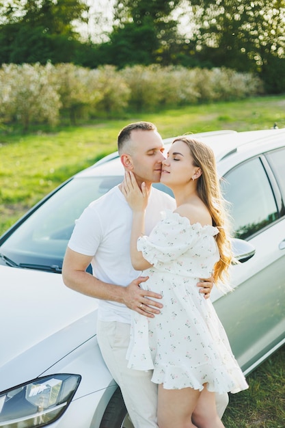 幸せな夫婦の妊娠の男女が開花したリンゴ園を歩く恋に落ちる自然の中の車を背景に恋をするカップル