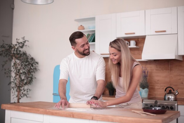 Happy married couple rolling out dough in the kitchen