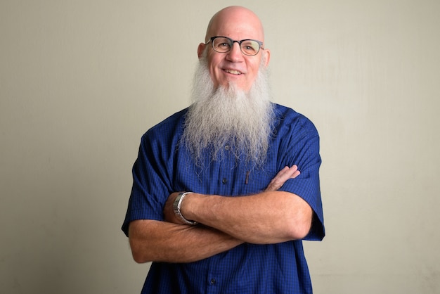 Happy mature bearded bald man smiling and wearing eyeglasses with arms crossed