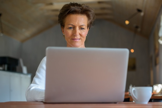 Happy mature beautiful woman with short hair using laptop inside coffee shop