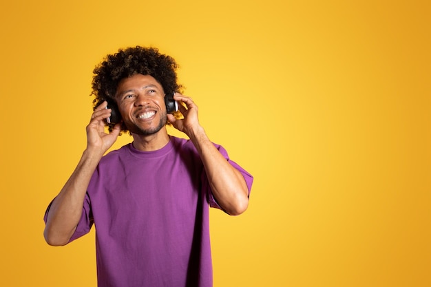 보라색 티셔츠와 무선 헤드폰을 쓴 행복한 성숙한 검은 곱슬머리의 남자는 음악을 즐긴다