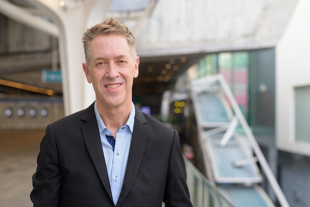 Happy mature businessman smiling at footbridge in the city