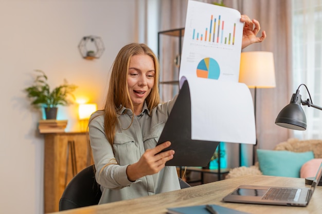 happy mature businesswoman freelancer analyzing graph documents sitting at home office table desk