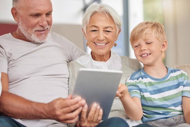 A happy mature couple bonding with their grandchild while babysitting and using a digital tablet on a couch at home Grandparents relaxing with their cute little grandson and browsing the internet