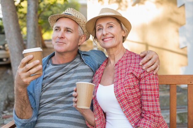 都市のベンチでコーヒーを飲む幸せな成熟したカップル