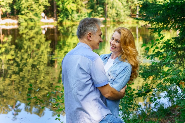 湖の近くの茂みの岬で抱きしめ、抱きしめる幸せな成熟したカップルは