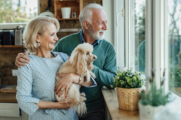 Happy mature couple enjoying with their dog by the window and looking through it