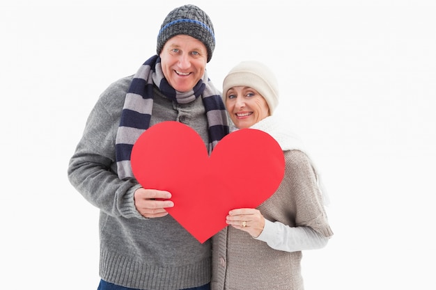 Happy mature couple in winter clothes holding red heart