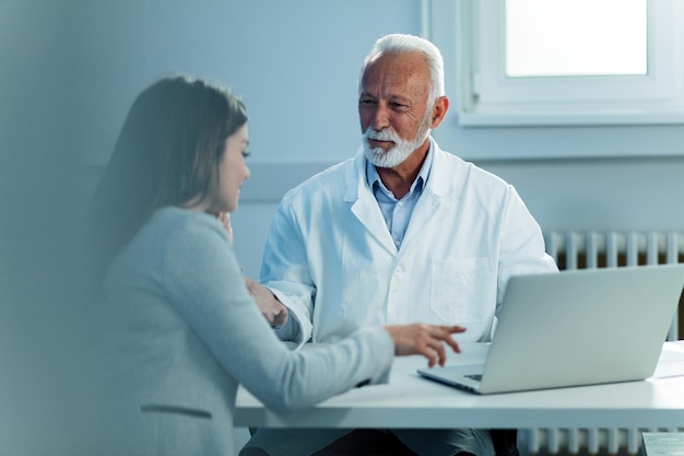 Happy mature doctor and his patient communicating while reading medical records at doctor's office