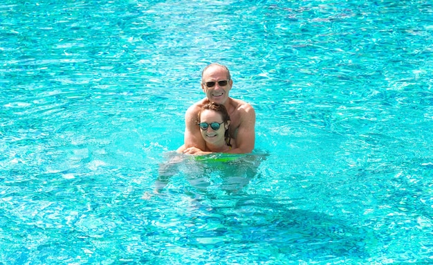 Happy mature family bonding couple have fun in outdoor swimming pool enjoying vacation and freedom