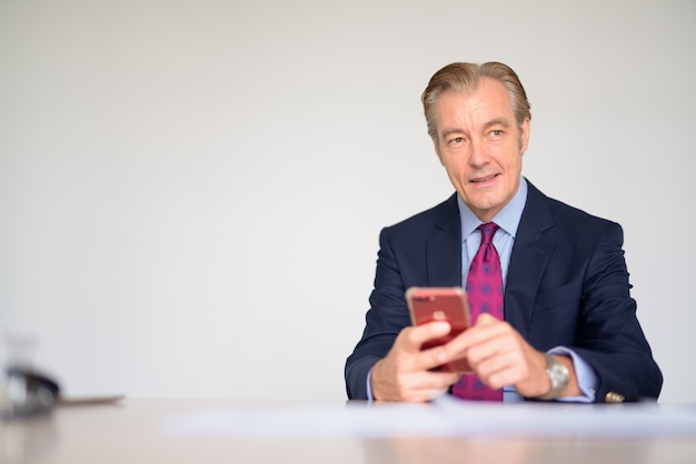 Happy mature handsome businessman thinking while using phone at work