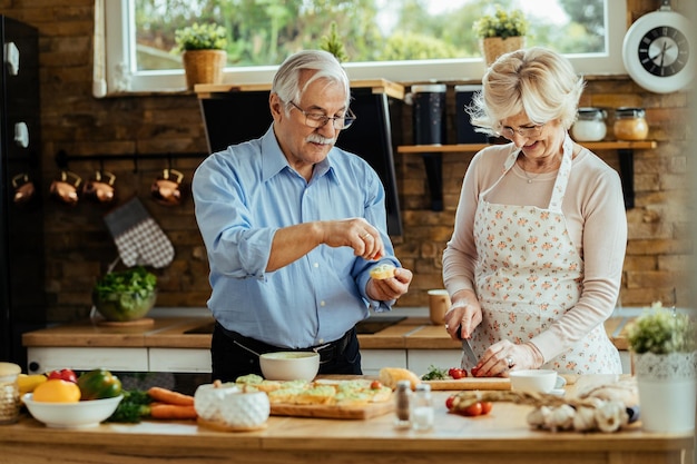 Happy mature husband and wife enjoying in preparing food in the kitchen