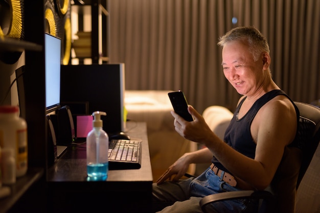 Happy mature Japanese man using phone while working from home