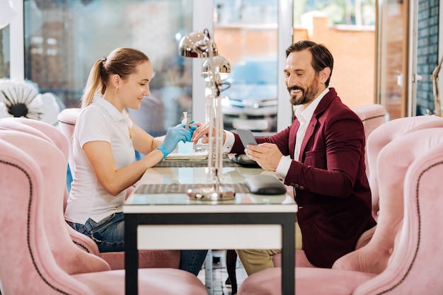 Happy mature man getting nails done and utilizing phone