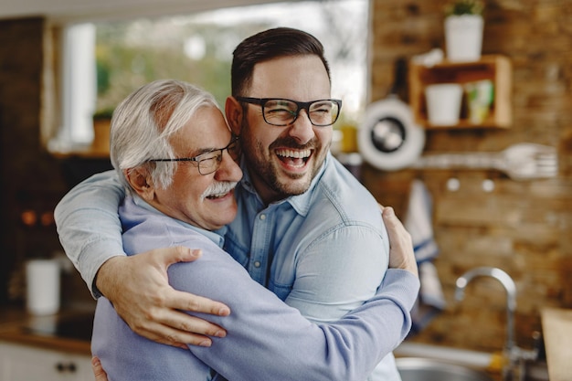 Happy mature man having fun while embracing with his adult son who came to visit him