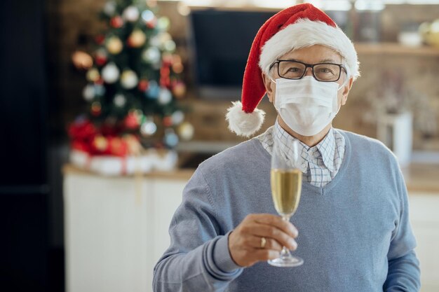 Happy mature man having glass of Champagne while celebrating Christmas at home due to COVID19 pandemic