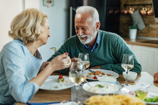 Happy mature man and his wife talking while having lunch together in dining room