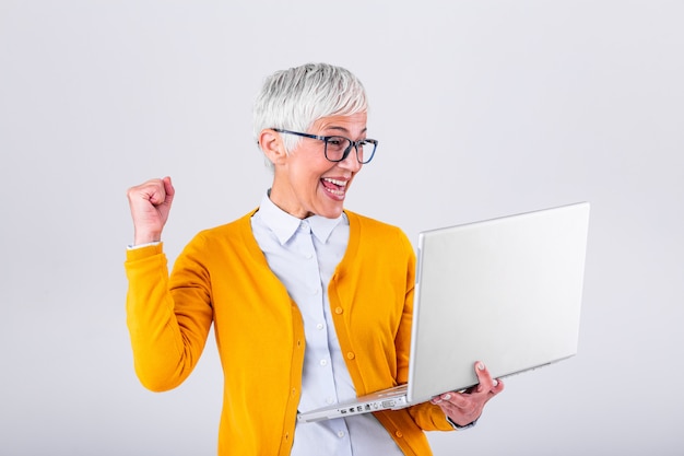 Happy mature middle aged elderly business woman winner excited by reading good news looking at laptop