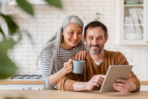 Photo happy mature middleaged family couple parents husband and wife checking emails reading news on digital tablet during breakfast choosing new house using application online