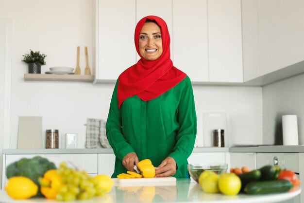 Happy mature muslim woman cooking making salad in kitchen