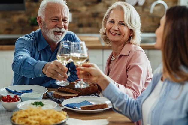 幸せな成熟した両親と彼らの大人の娘は、ダイニングルームで昼食時にワインで乾杯します。フォーカスは成熟した女性です。