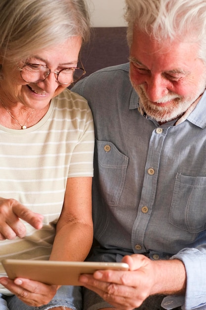 Happy mature people using digital online tablet together Elderly lifestyle people with technology in indoor leisure activity together Man and woman surfing the web and smiling sitting on sofa