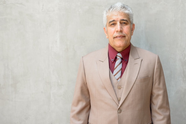 Happy mature Persian businessman with gray hair against concrete wall outdoors