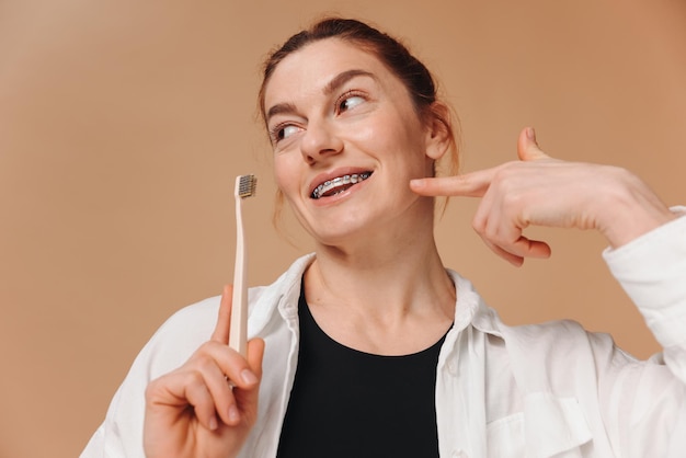 Happy mature woman in braces holding a toothbrush on a beige background