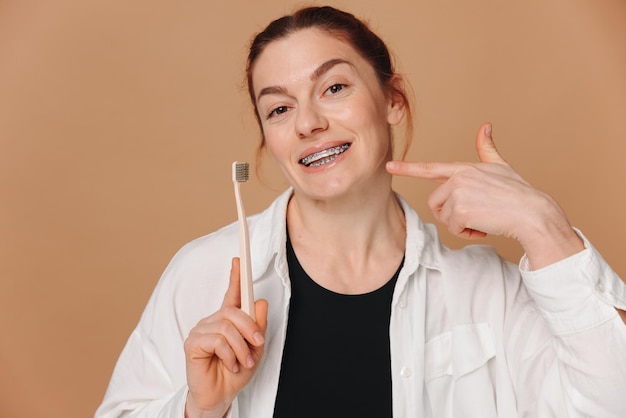 Happy mature woman in braces holding a toothbrush on a beige background