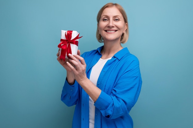 Happy mature woman holding bonus gift on blue background copy space