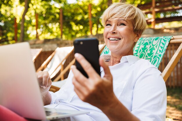 Happy mature woman holding mobile phone while resting