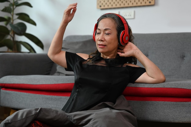 Happy mature woman listening to music on wireless headphones relaxing at home