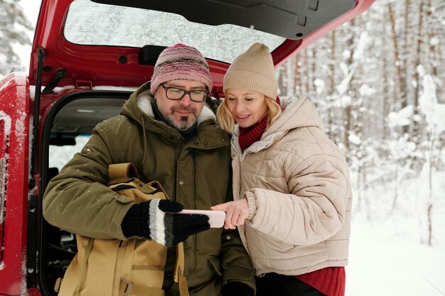 Happy mature woman pointing at screen of smartphone held by her husband