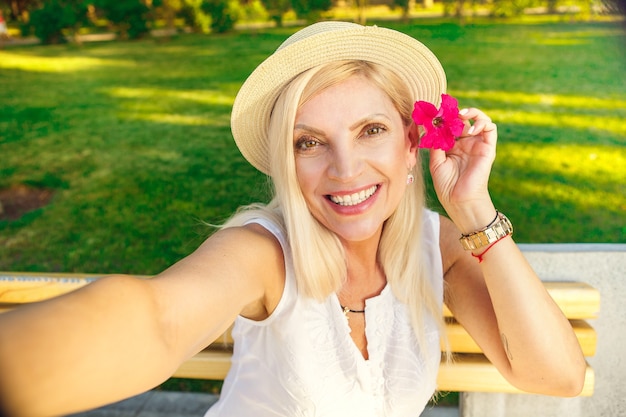 写真 彼女の髪に花と笑顔でポーズをとって自分撮りをしている幸せな成熟した女性