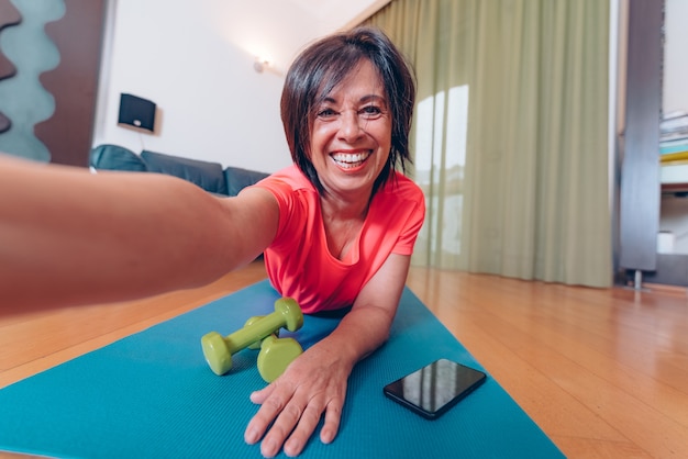 Happy mature woman taking a selfie at workout gym at home