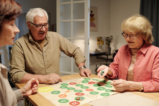 Donna matura felice che lancia i dadi dei cubi sopra il bordo di carta del gioco di svago