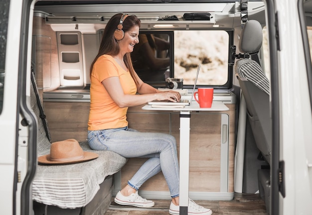 Happy mature woman using computer laptop inside mini van camper