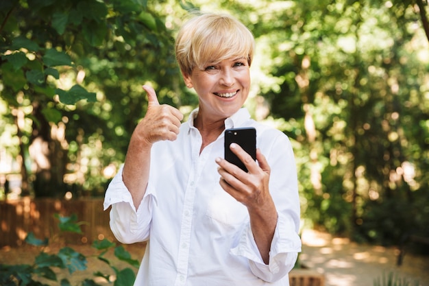 Donna matura felice che per mezzo del telefono cellulare