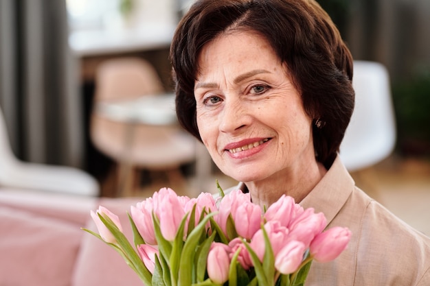 Счастливая зрелая женщина с букетом розовых тюльпанов, глядя на вас