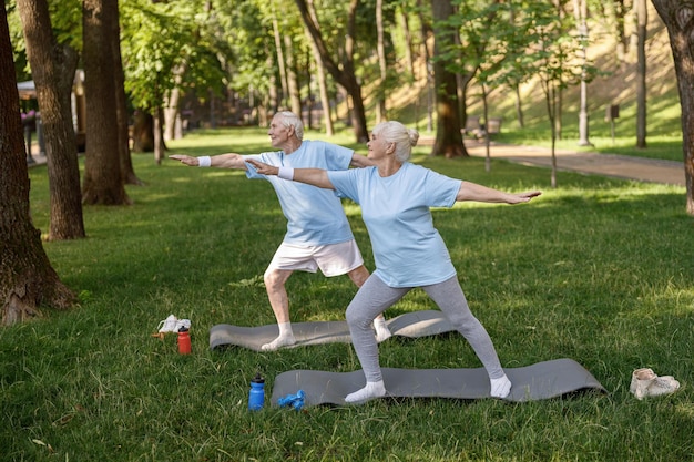 Happy mature woman with partner do yoga exercises on lush lawn