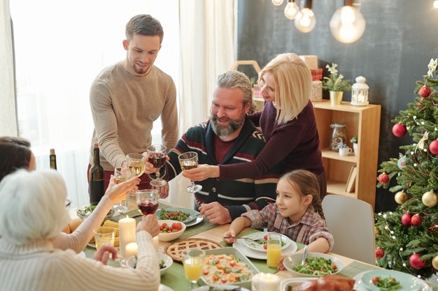 Happy mature and young couples toasting with glasses of wine over homemade food on festive table during xmas dinner