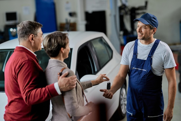 Happy mechanic getting car keys from a couple while working at auto repair shop