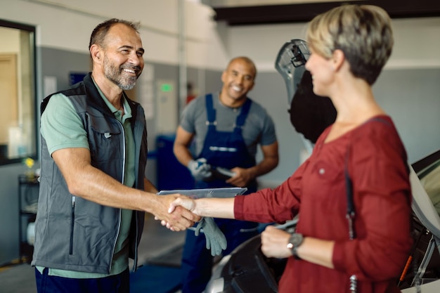 Foto stretta di mano felice del meccanico con il cliente femminile nell'officina riparazioni auto